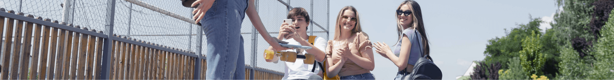 Een groep tieners die buiten staan, met een persoon die een skateboard vasthoudt en een ander die naar een telefoon kijkt.