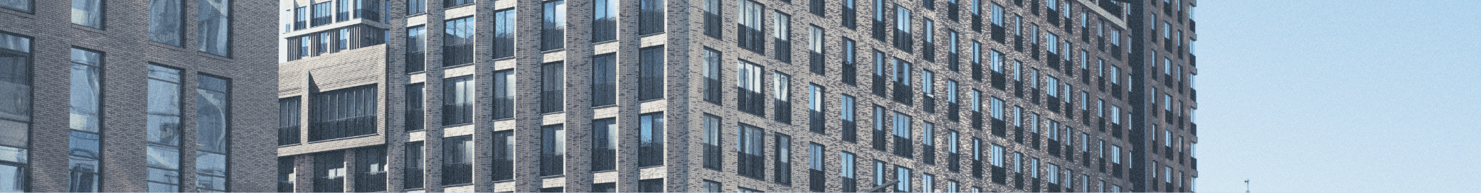 Een hoog, modern appartementencomplex met grote ramen en een heldere blauwe lucht op de achtergrond.